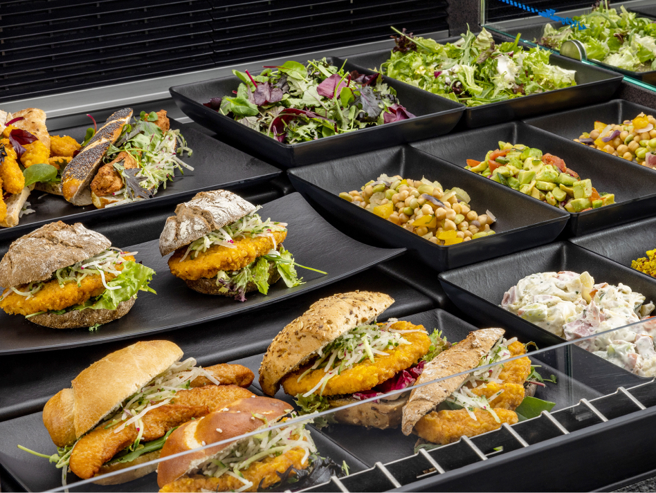 Snacks und Salate auf schwarzen Schalen in der Frischetheke.